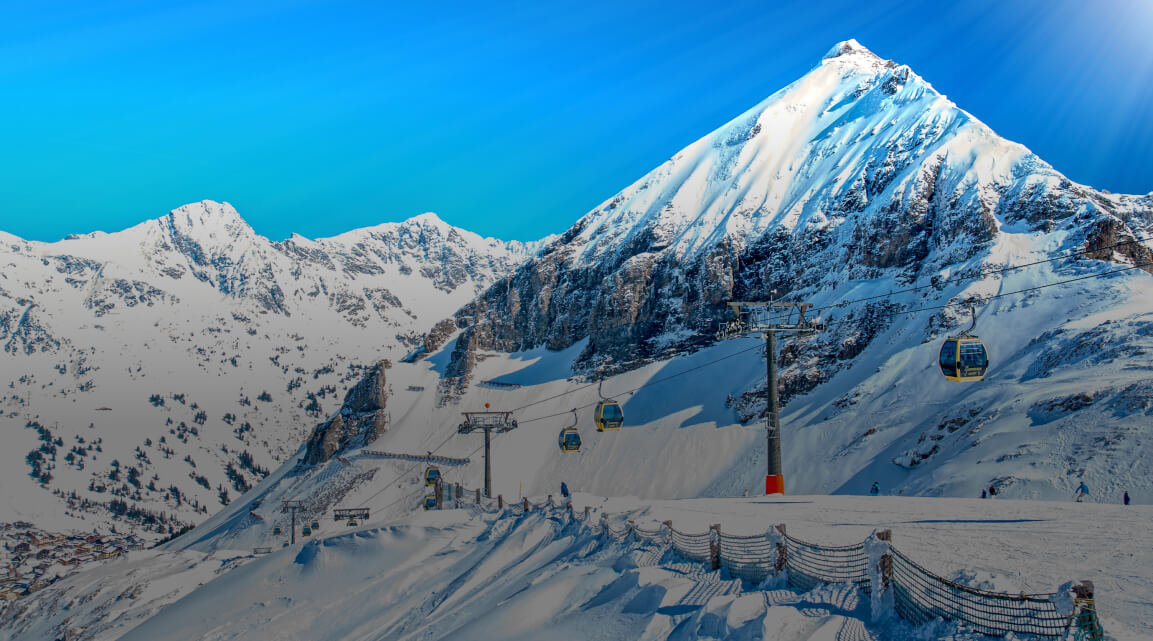A ski lift on a picturesque snow-covered mountain with a huge peak rising against a brilliant blue sky