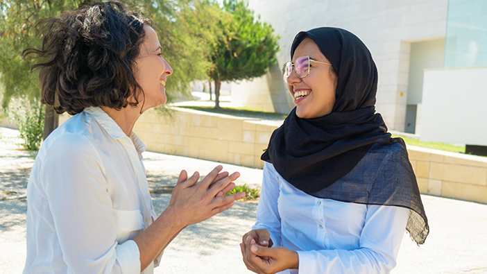 Two women standing outside laughing and talking 