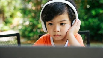 A child sitting outside wearing headphones looking at a computer
