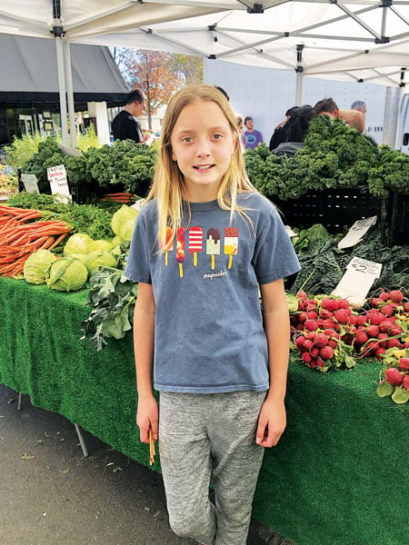 A girl wearing an Esri T-shirt posing in front of a vegetable stand