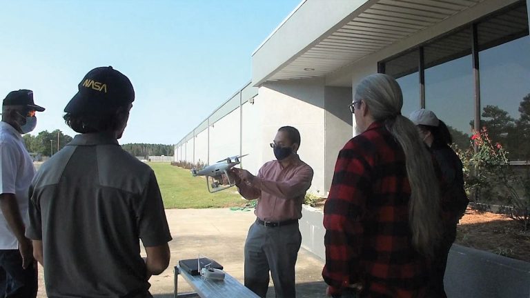 Dr. AdegokeAdemiluyi showing students a white UAV outside of a building