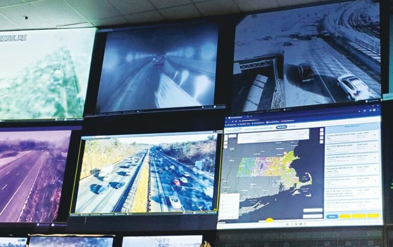 Several screens on a wall showing live videos of traffic next to a map-based dashboard