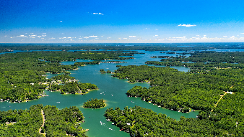 Boats ply a waterway surrounded by a forested area under blue skies.