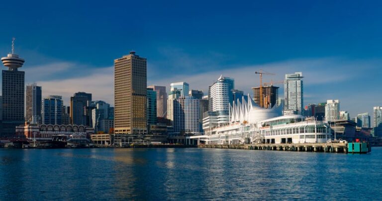 Tall buildings next to water with a conference center with sails for a roof jutting out into the bay