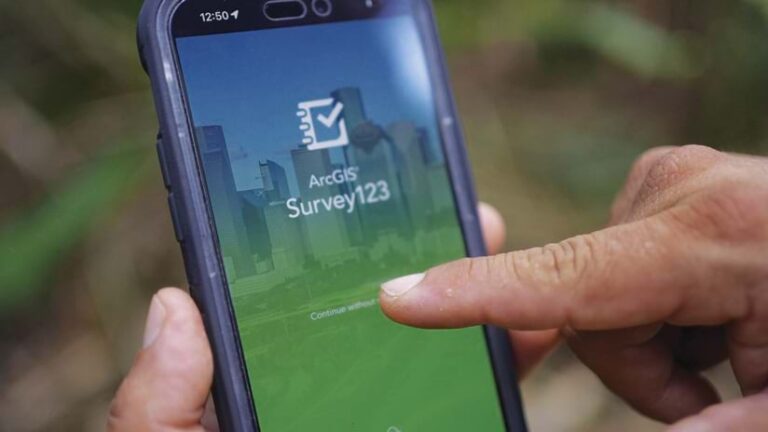 A close up of a person holding a smartphone that has the ArcGIS Survey123 welcome screen on it, with one of that person’s fingers tapping the “continue” button