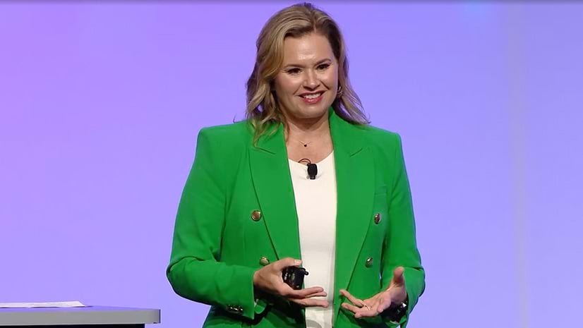 A person wearing a green jacket and smiling in front of a lavender background