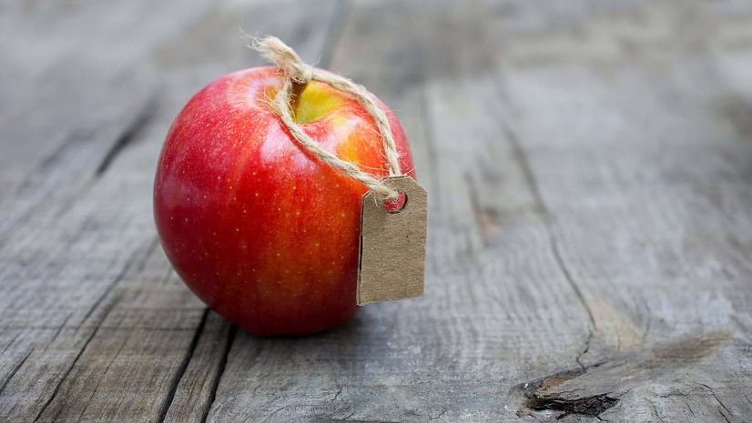 A red apple with a brown tag sits on a faded wooden surface