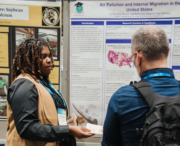 With an infographic in the background, an individual hands a paper to another.