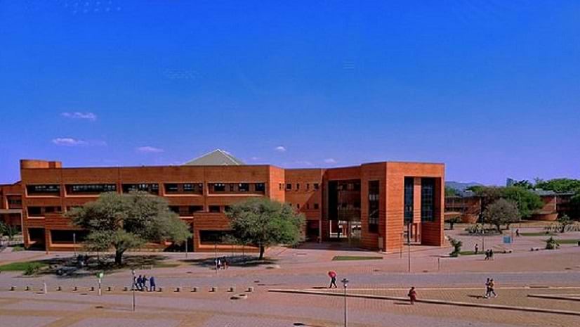 People walk on mostly paved areas near an orange-colored building