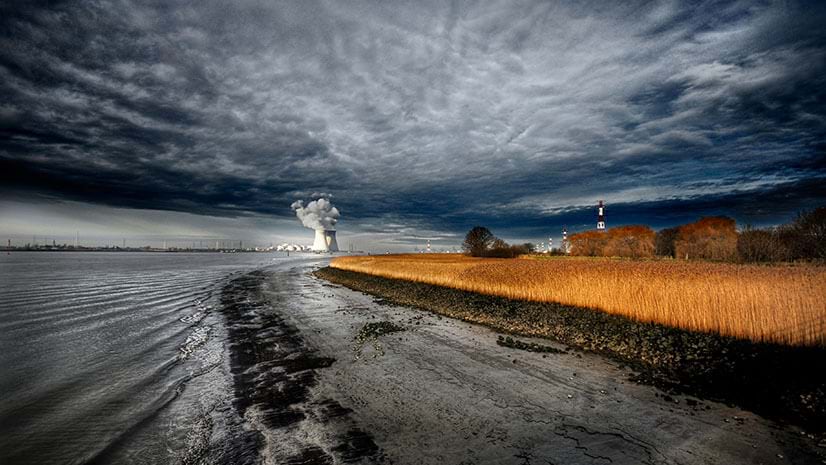 A nuclear power plant under cloudy skies with river and fields in foreground