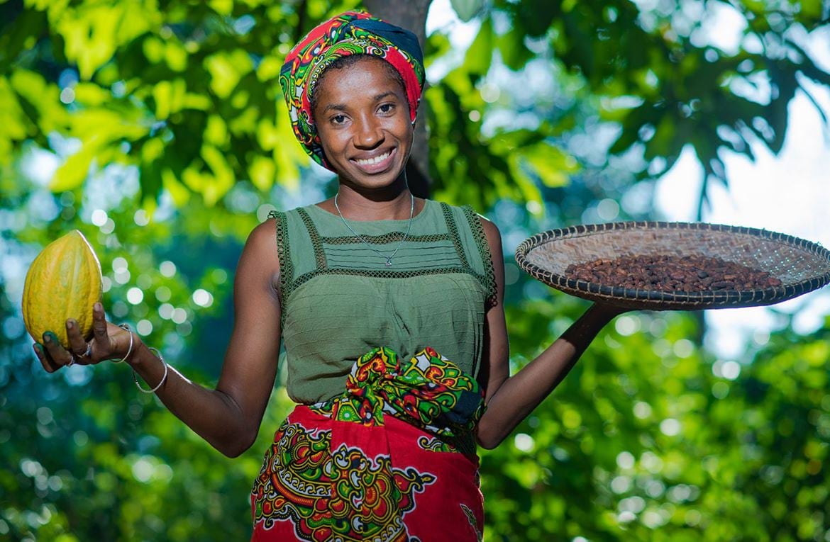 A woman, with green trees as a background, holds bowls of food