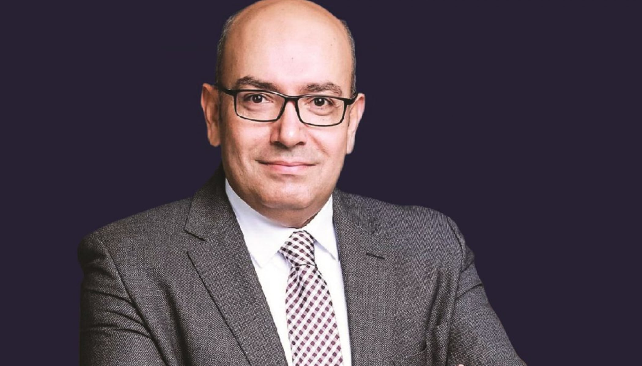 A portrait of Sohail Elabd in glasses and a gray suit with a flat black background