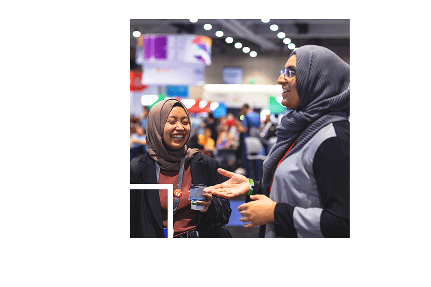 Duas mulheres em hijabs rindo e sorrindo no salão de exposições em uma conferência
