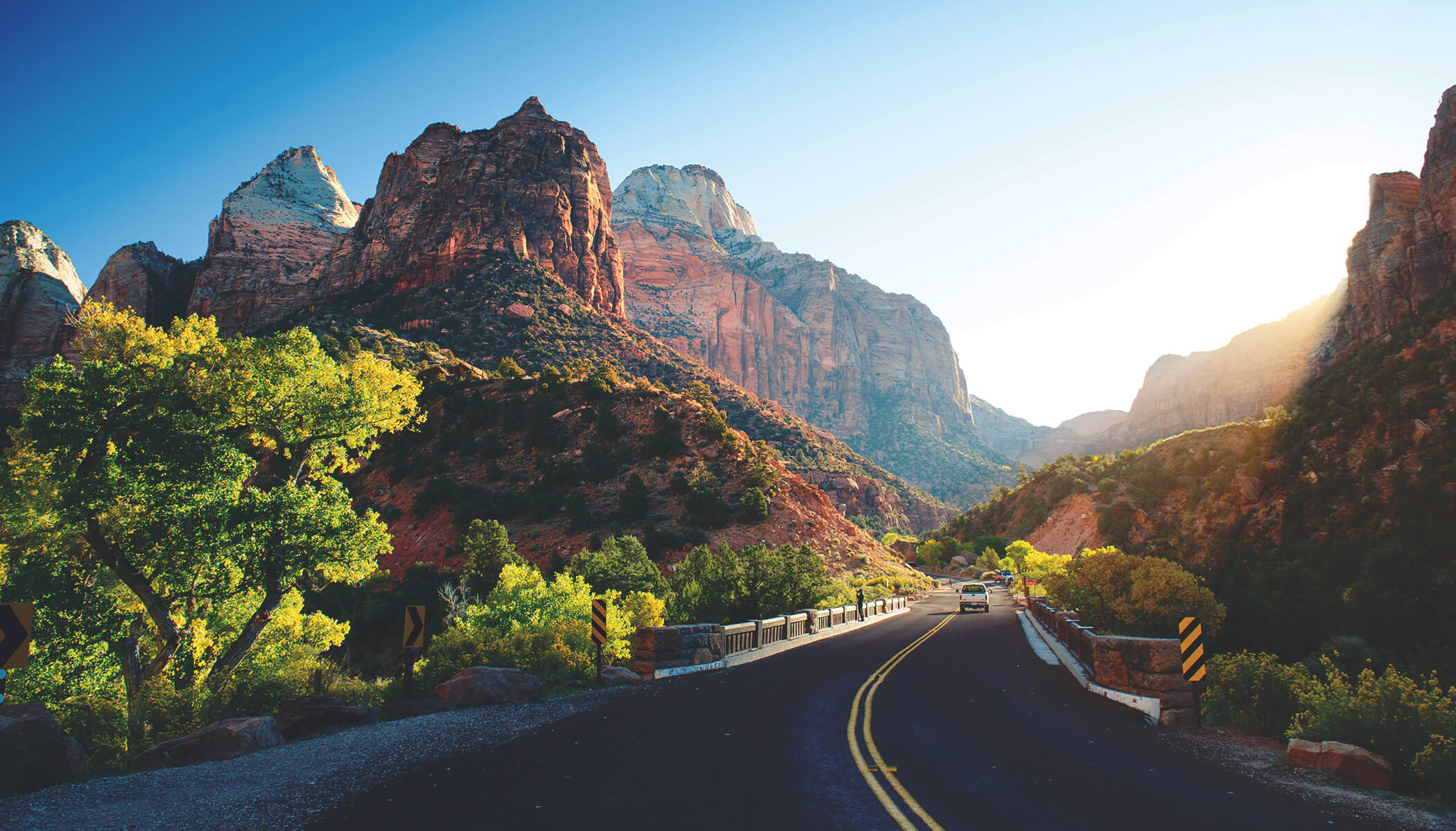 A two-lane road bisecting a canyon surrounded by buttes under a clear, blue sky