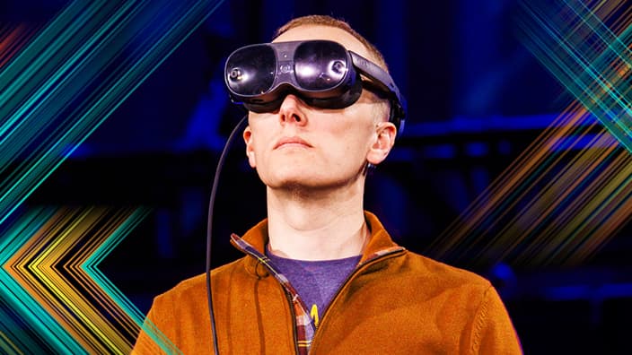 Head and shoulders portrait of a person wearing an orange zip up sweater and a virtual reality headset over their eyes