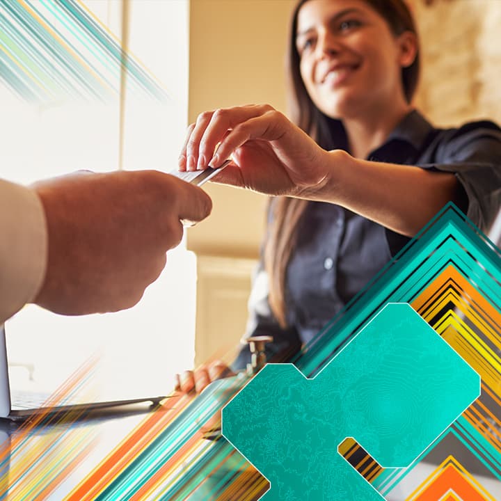 Smiling hotel desk clerk handing a key card to a guest