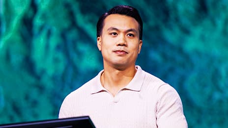 Presenter in a light-colored polo shirt against a teal and blue topographical map