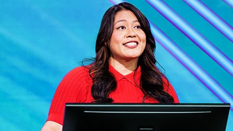 Presenter with long dark hair standing behind a podium wearing a vibrant red blouse