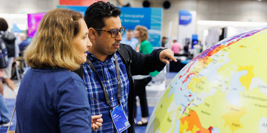 Two event attendees engaged in discussion in front of a large colorful globe in the Expo