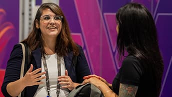 An animated and smiling event attendee facing forward engaged in conversation against a colorful pink and purple backdrop