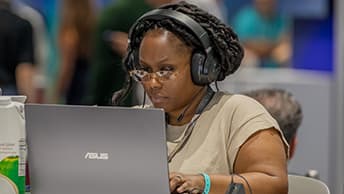 Deeply focused event attendee wearing over the ear headphones while using a laptop