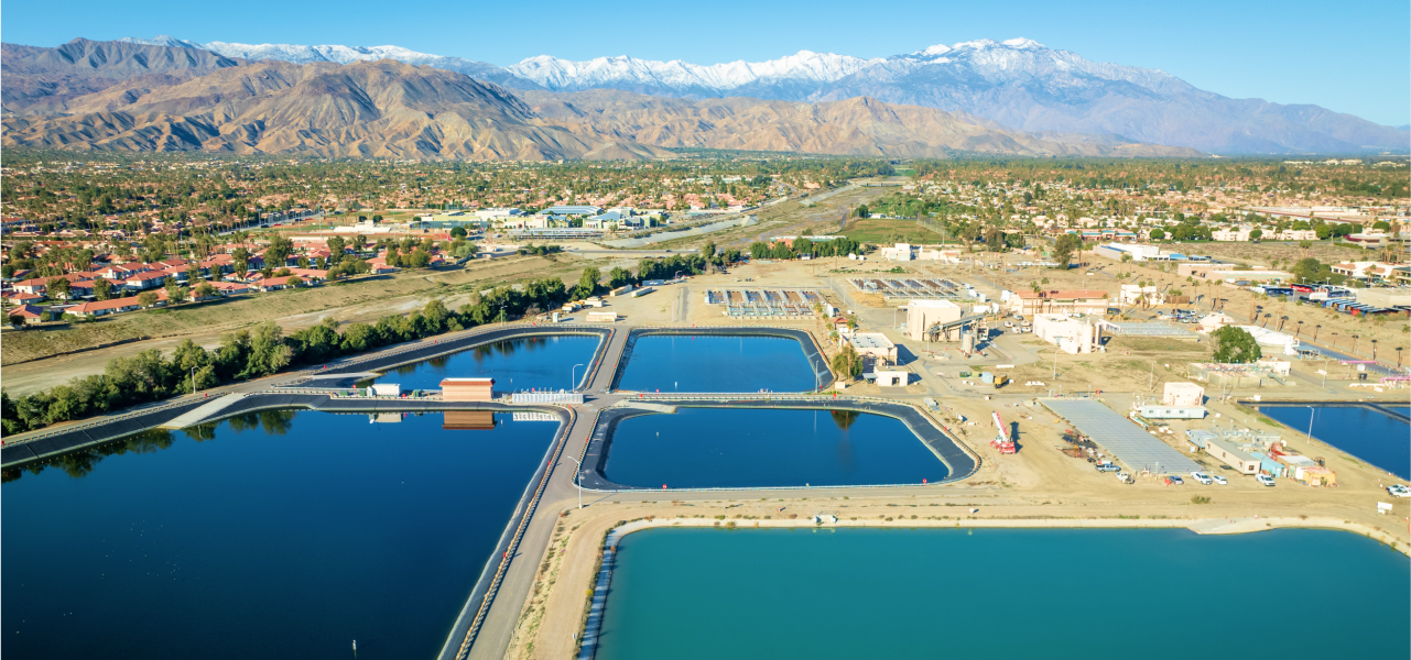 Aerial view of a water treatment facility in a desert landscape with snow-capped mountains in the distance