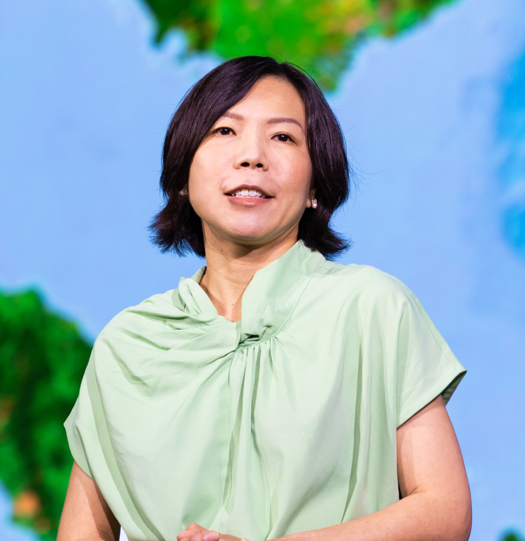 Event presenter with chin-length dark hair wearing a pale green blouse standing in front of a blue and green map