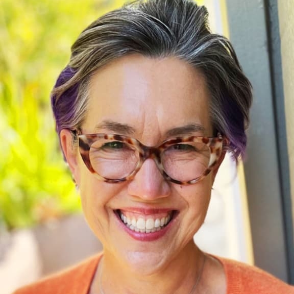 Sarah McDonald smiling, wearing an orange button up sweater and tortoiseshell glasses.