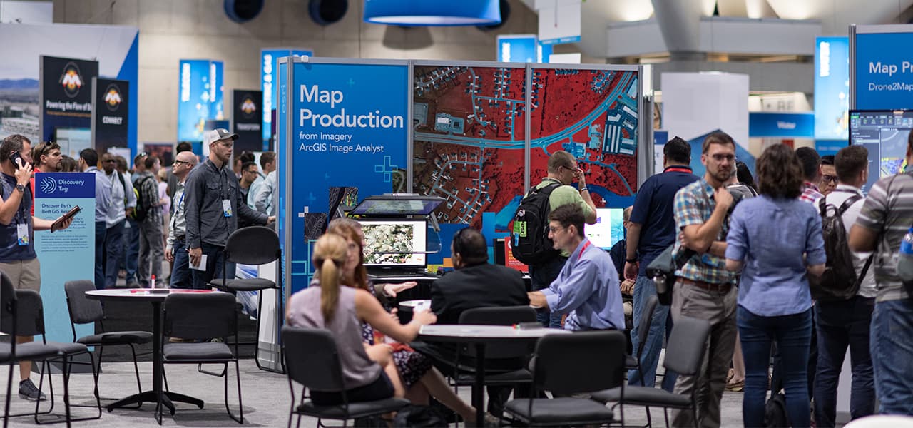 Attendees and Esri experts gathered in the Expo Hall seated at tables and engaged in conversation at various industry booths