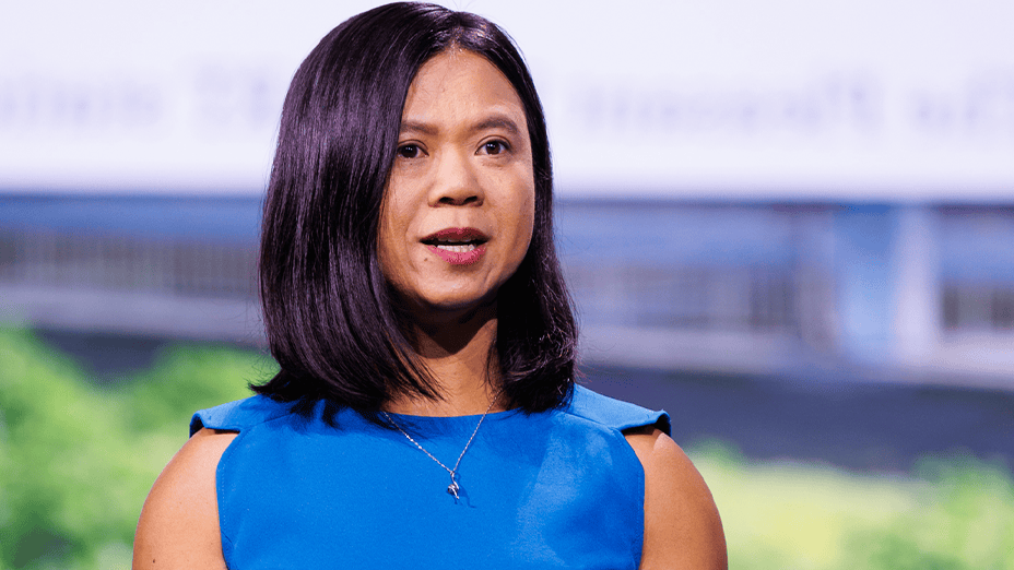 Portrait of a presenter with shoulder-length dark hair wearing a blue blouse