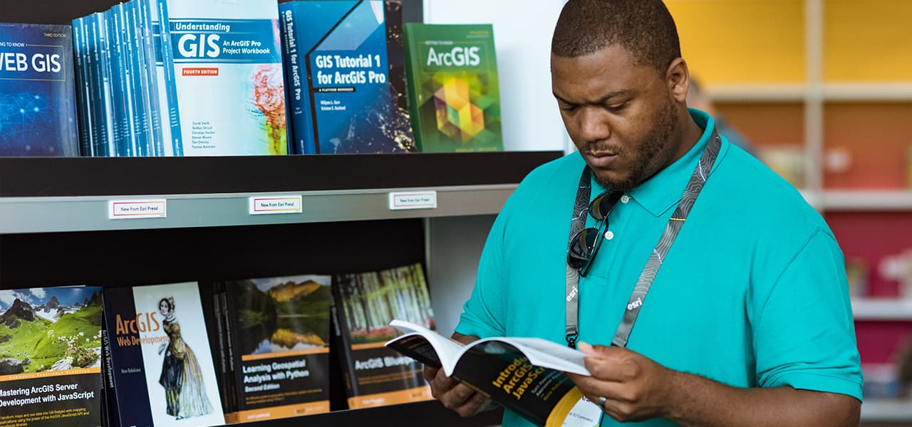 Person wearing an aqua blue polo shirt examining a book at the Esri Press booth