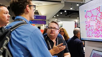 Exhibitor explaining a diagram on a monitor to two Expo attendees