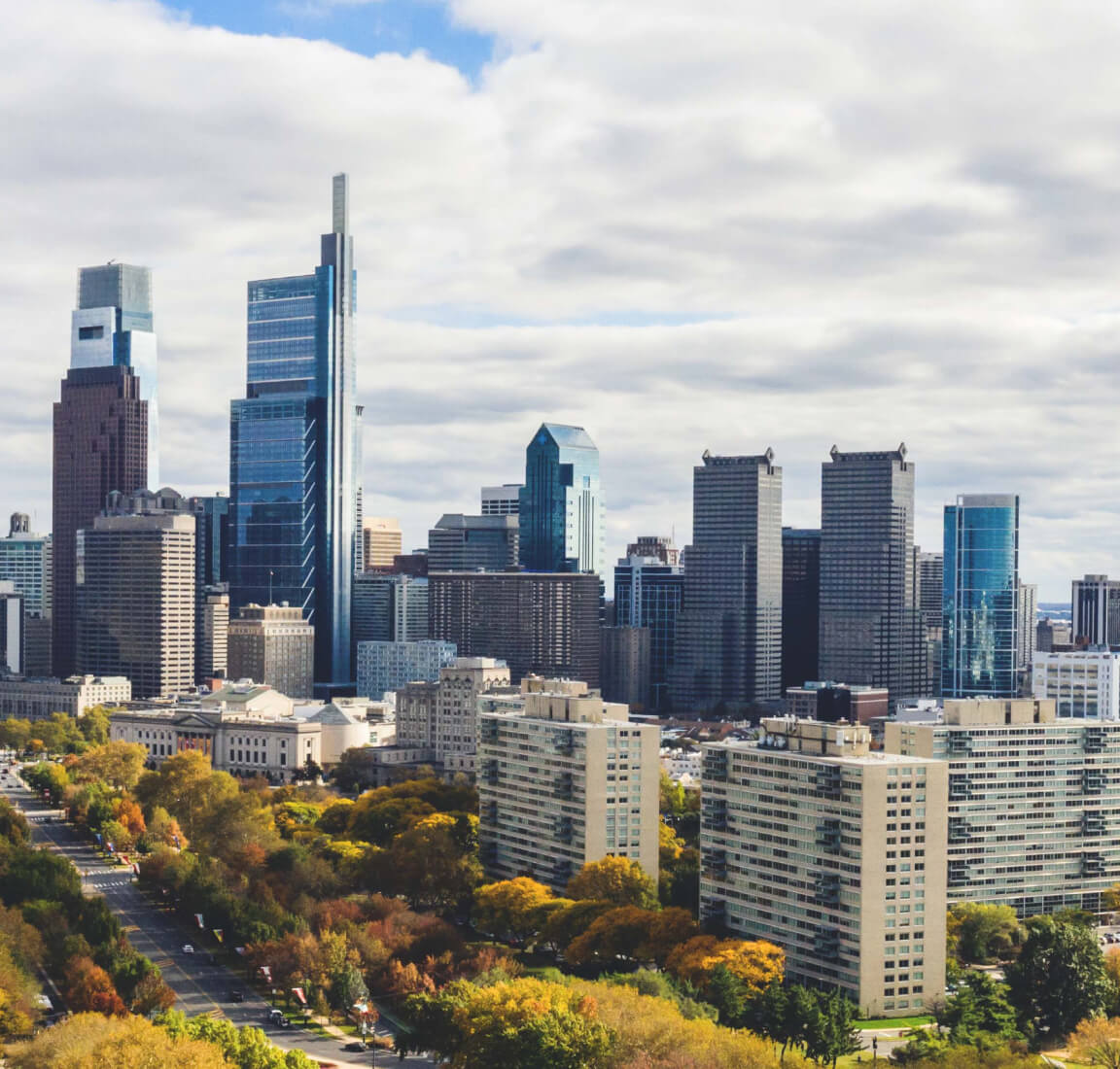 Photograph of the Philadelphia skyline with large buildings and autumn trees