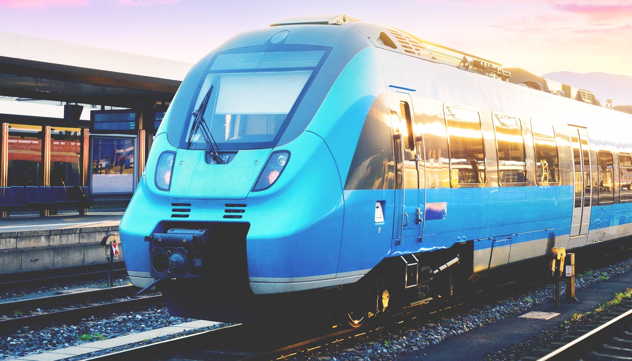 A blue subway train resting at an outdoor subway station with the windows reflecting golden morning sun