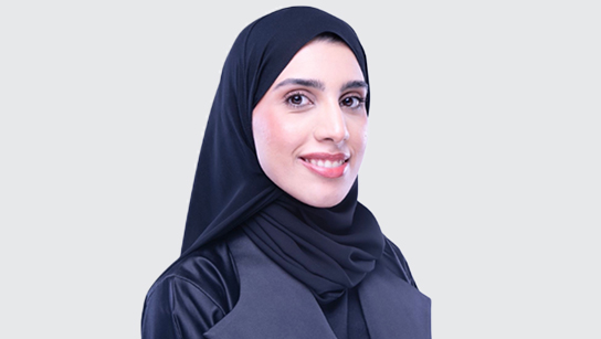 Portrait of Hajar smiling in a dark indigo hijab and navy blue blouse with a plain white background