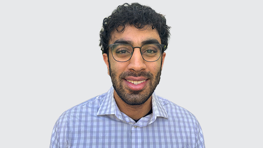 Portrait of Kavin smiling in a light blue plaid shirt with a plain white background