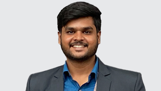 Portrait of Radhakrishnan smiling in a bright blue collared shirt and gray blazer with a plain white background