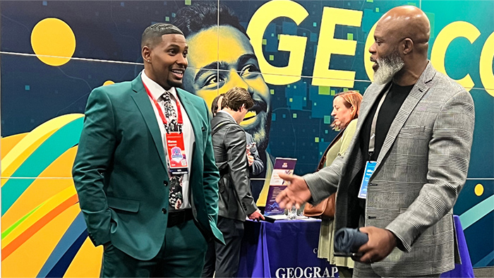 Two conference attendees wearing suits standing in an exhibit hall chatting