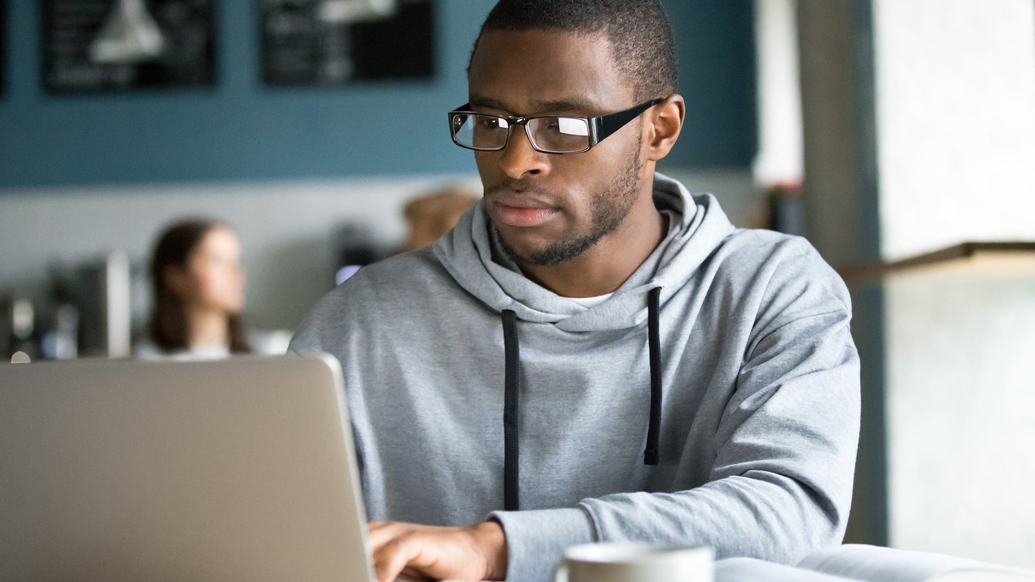 A person wearing a gray hooded sweatshirt concentrating on a laptop display in a home office