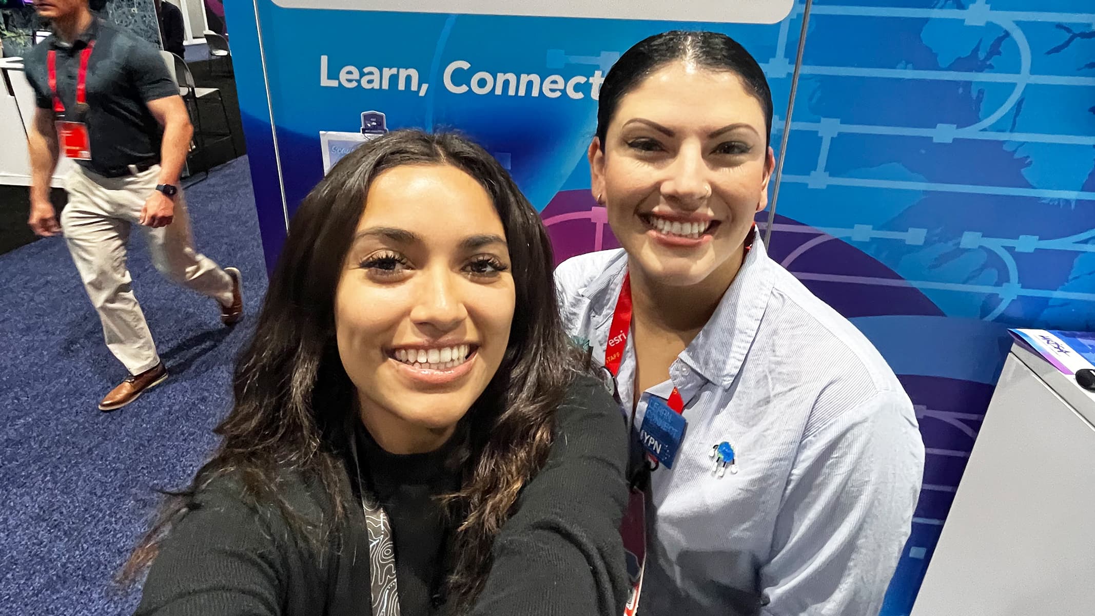 Two business professionals wearing conference lanyards at an event, smiling for a candid photo