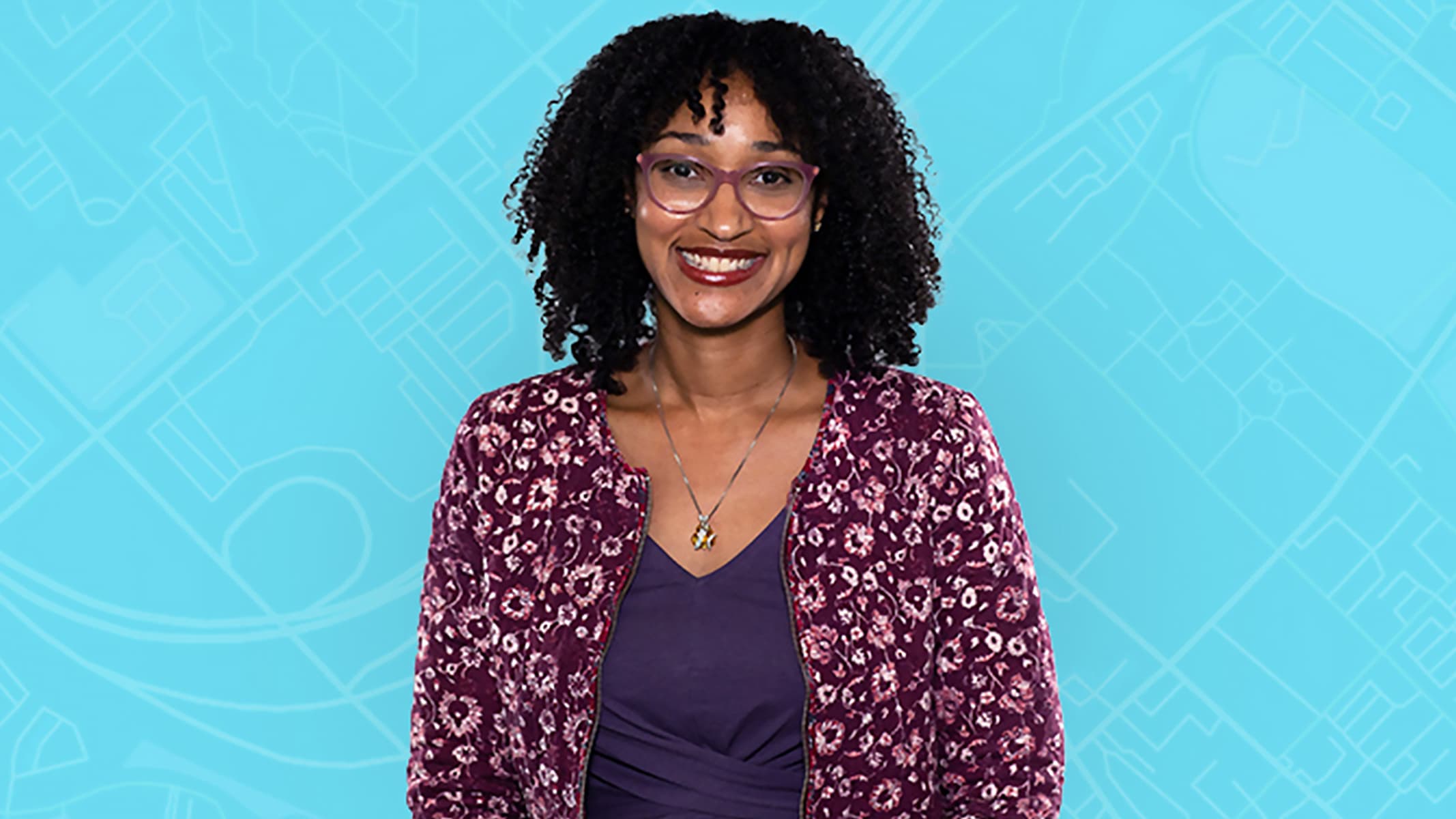 A smiling person wearing a casual purple blouse and flowered jacket"