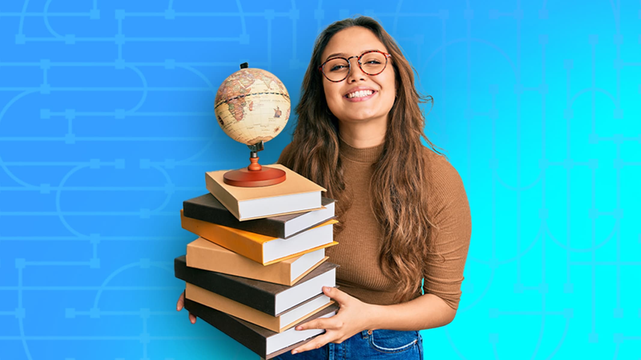 A smiling person in a brown sweater and jeans holding a stack of books with a small globe on top