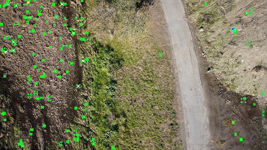 Imagerie par drone représentant le paysage à côté d’une petite route, avec des points verts là où un modèle de Machine Learning a identifié des déchets