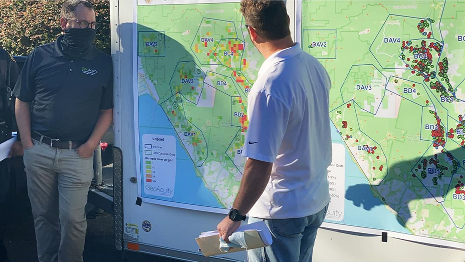 Dos hombres mirando un gran mapa impreso que muestra los puntos críticos de incendios forestales como polígonos rojos