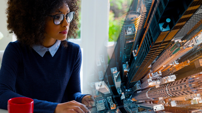 Immagine composita di una persona con un pullover blu che usa un computer in un ufficio luminoso accanto a una foto aerea di moderni grattacieli