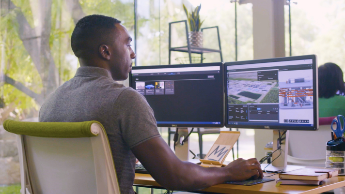 Homem sentado em frente a dois monitores em um escritório trabalhando com dados 3D para modelar um edifício