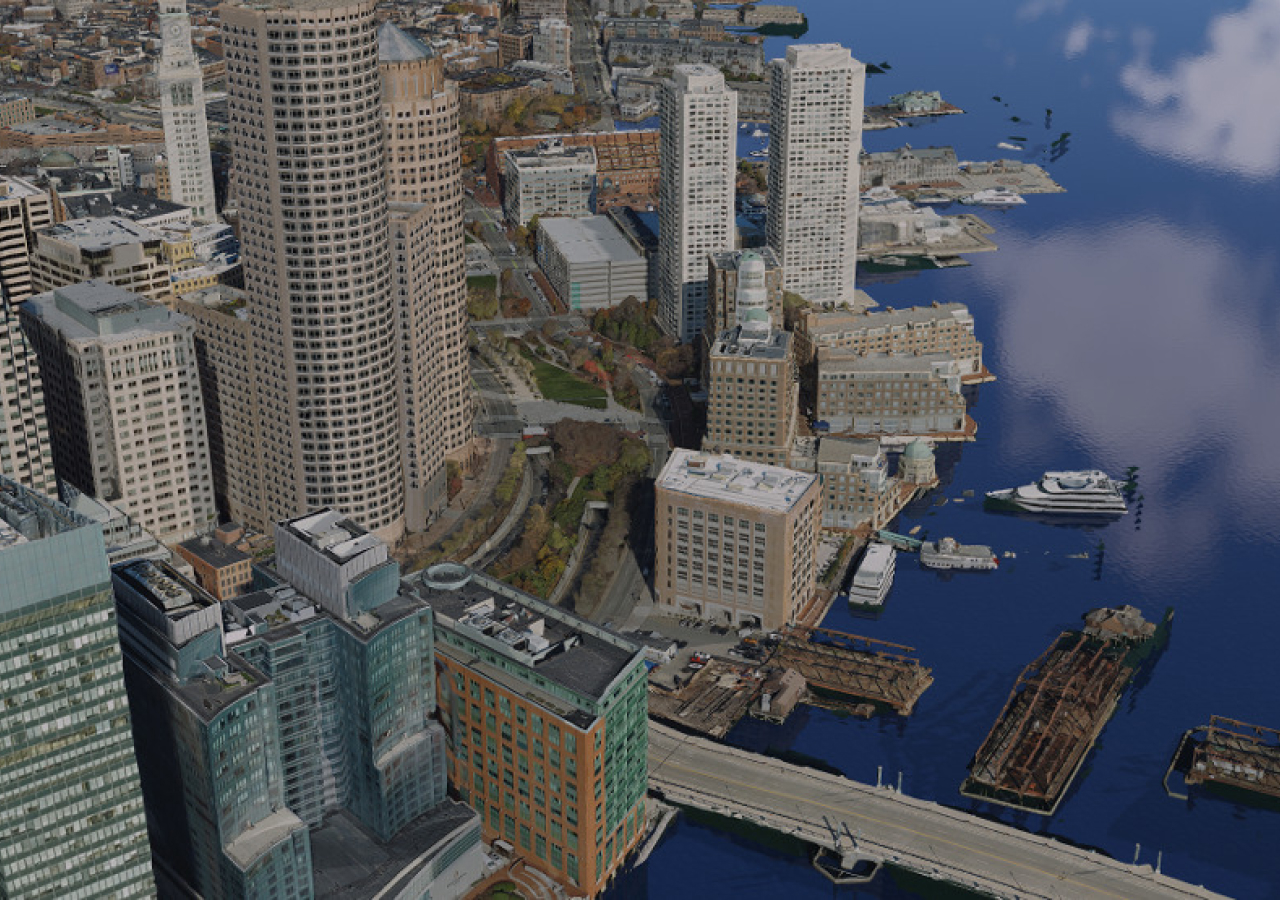 Luftbild einer Stadt am Wasser mit hohen Gebäuden und mit Booten und Lastkähnen im blauen Wasser
