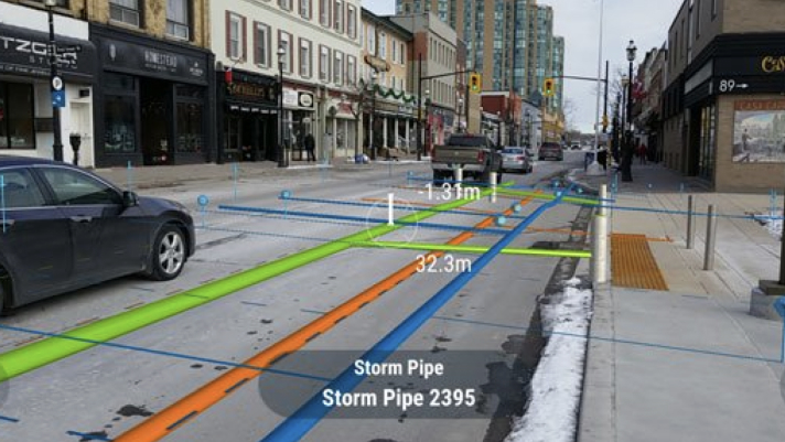 : View of cars driving down a road lined with stores, with virtual renderings of storm pipes and their numerical measurements