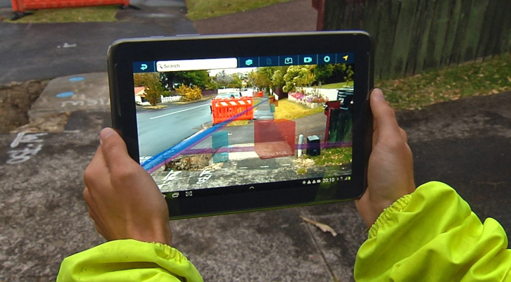 Руки держат iPad на улице, на котором изображена строительная площадка, чтобы визуализировать пространственный контекст 