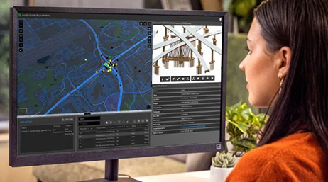 A person sitting in front of a desktop computer screen displaying a map, a 3D model, and other data